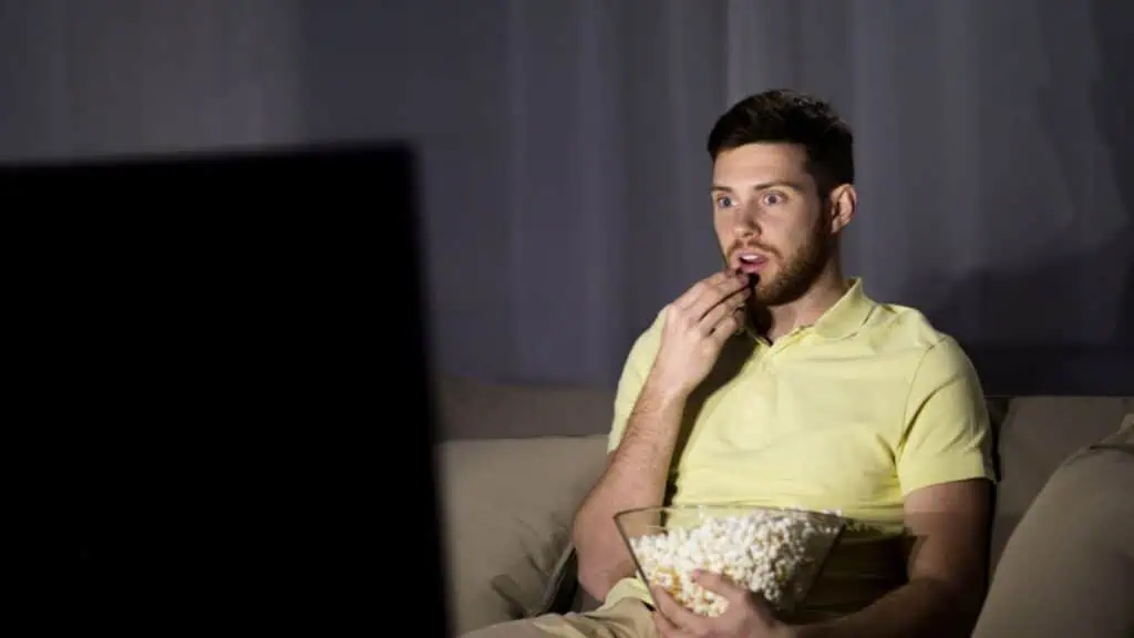 Man watching tv and eating popcorn at night