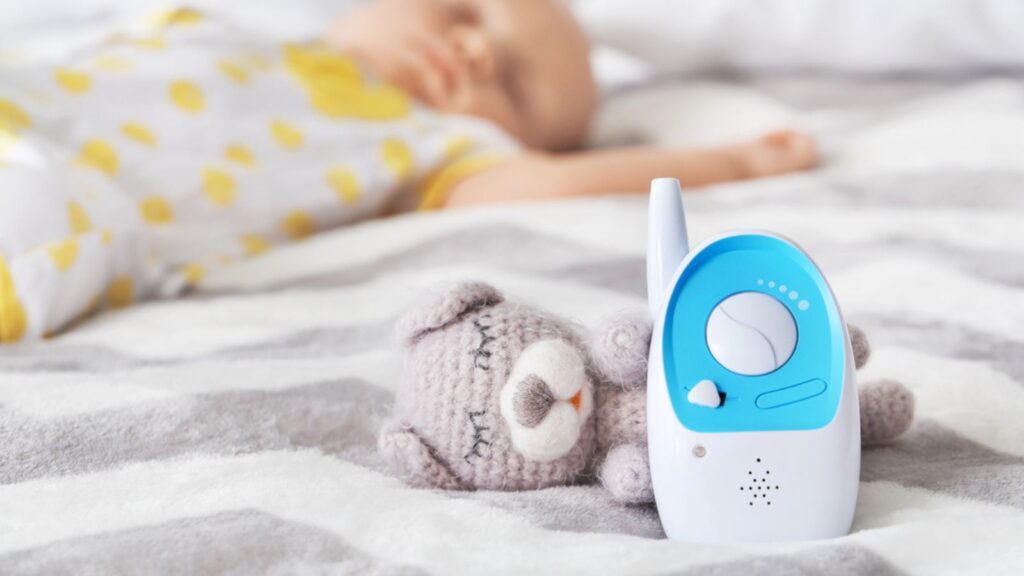 Modern baby monitor and toy on bed of sleeping infant