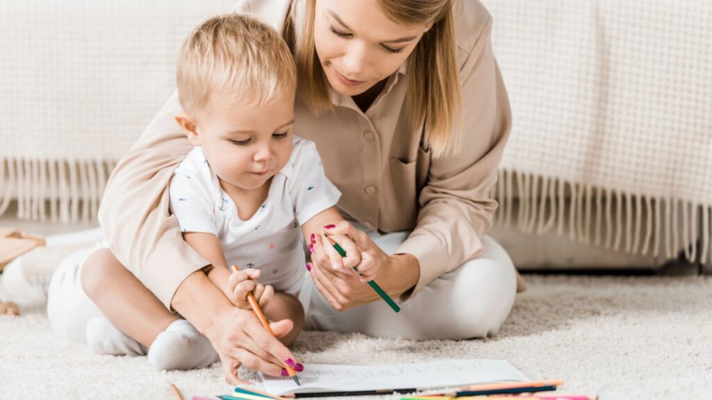 Mother and adorable toddler drawing together in nursery room