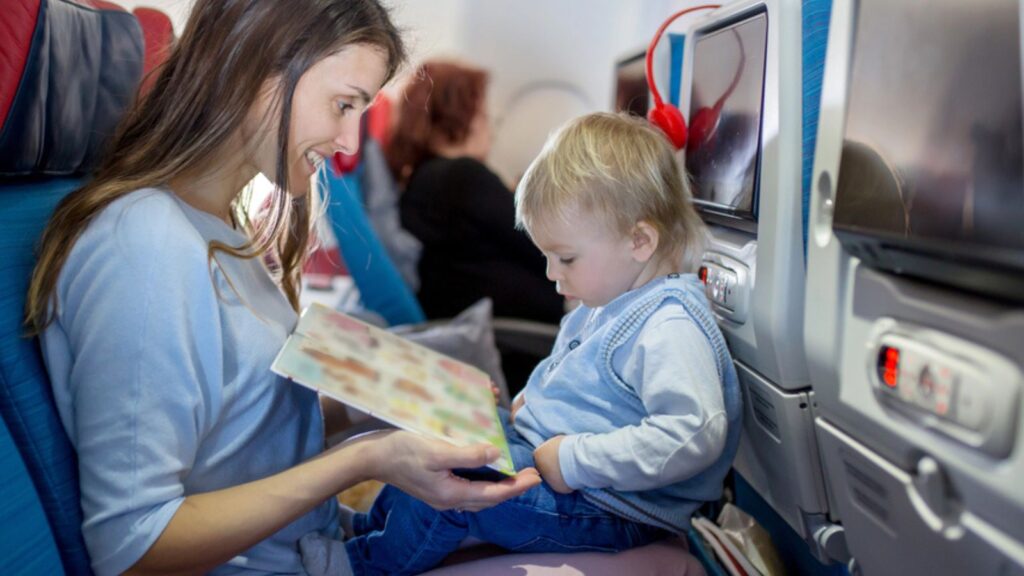 Mother, entertaining little toddler boy on board of aircraft on