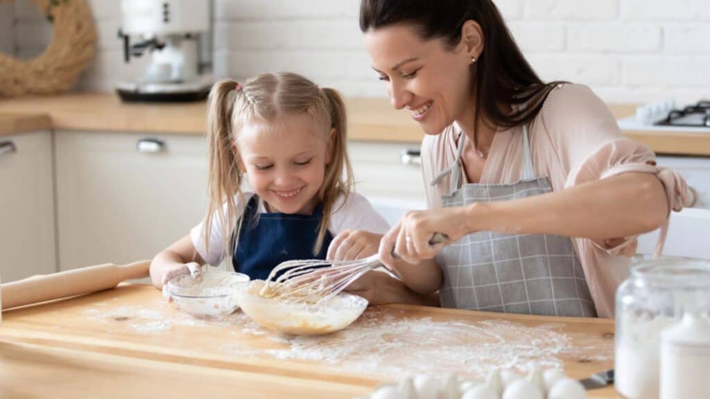 Mother showing small daughter how to stir eggs
