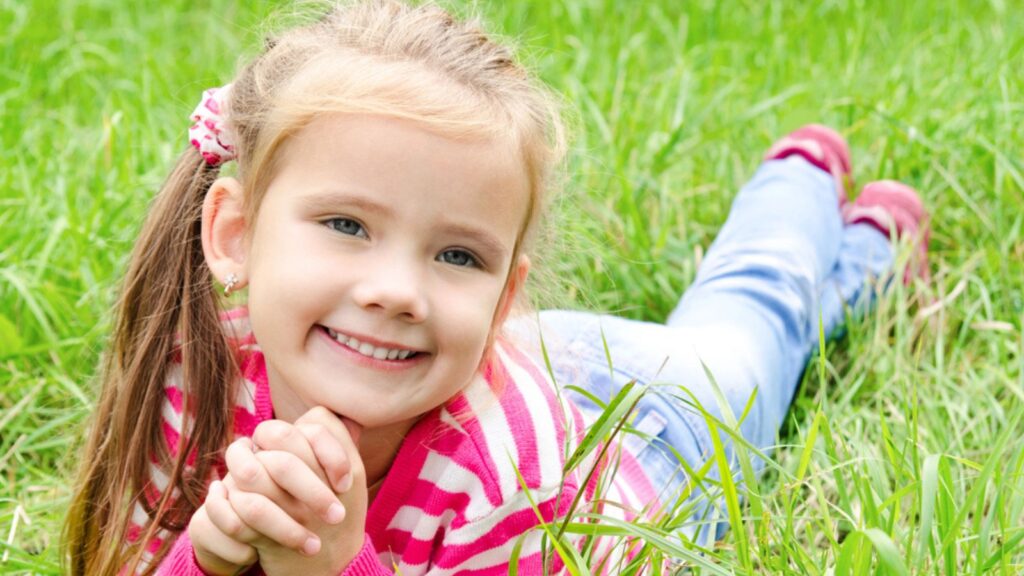 Portrait of adorable smiling little girl lying on grass