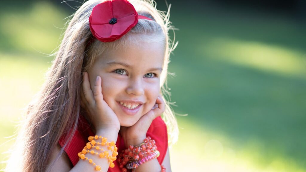 Portrait of happy pretty child girl smiling outdoors enjoying warm sunny summer day with red headband