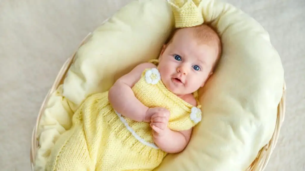 Portrait of newborn baby girl lying in a basket with golden crown and yellow bodysuit