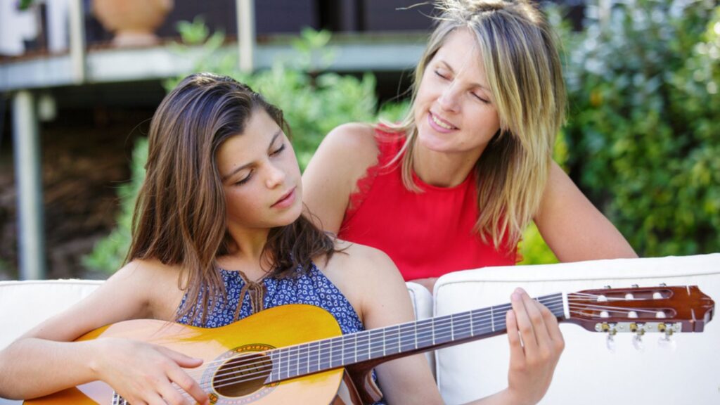 Pretty girl playing guitar in a garden with her mom
