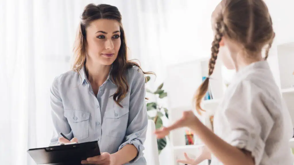 Psychologist woman with clipboard talking to little child