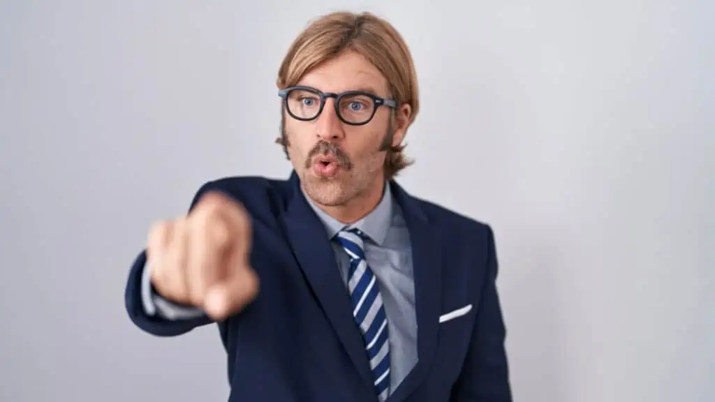 Rude man with mustache wearing business clothes pointing with finger surprised ahead