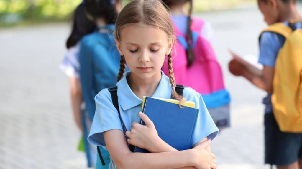 Sad little girl and her classmates outdoors