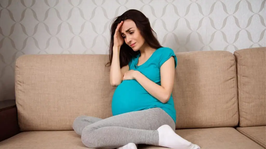 Sad pregnant woman sitting at the couch
