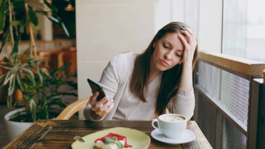 Sad woman sitting alone in coffee shop at table with cup of cappuccino