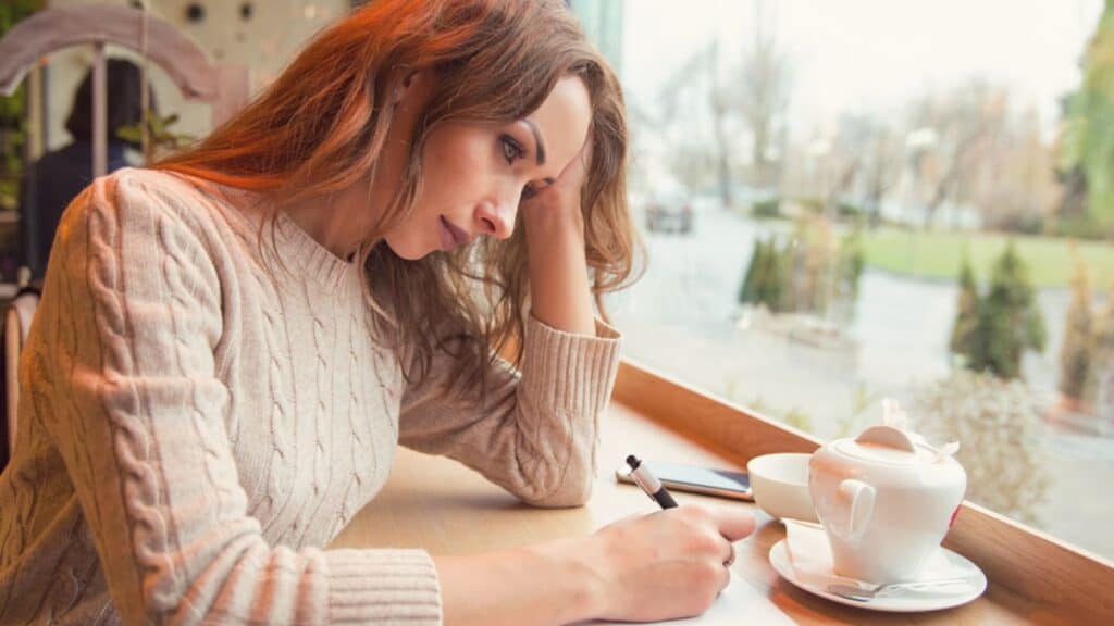 Sad young woman writing letter with broken heart feeling desperate