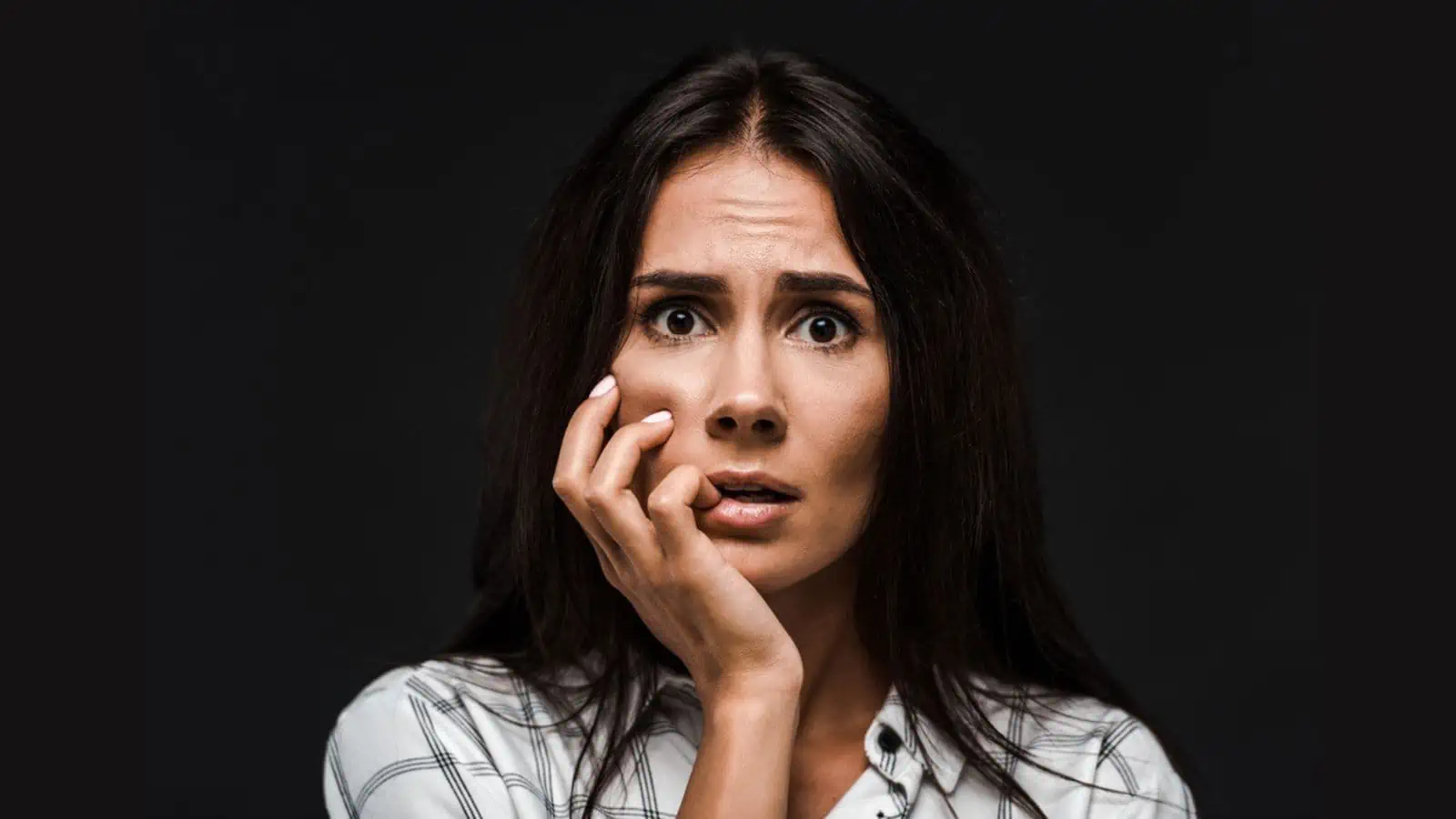 Scared young woman touching face isolated on black