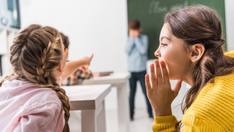 Selective focus of school girl gossiping while classmate pointing with finger at upset school boy