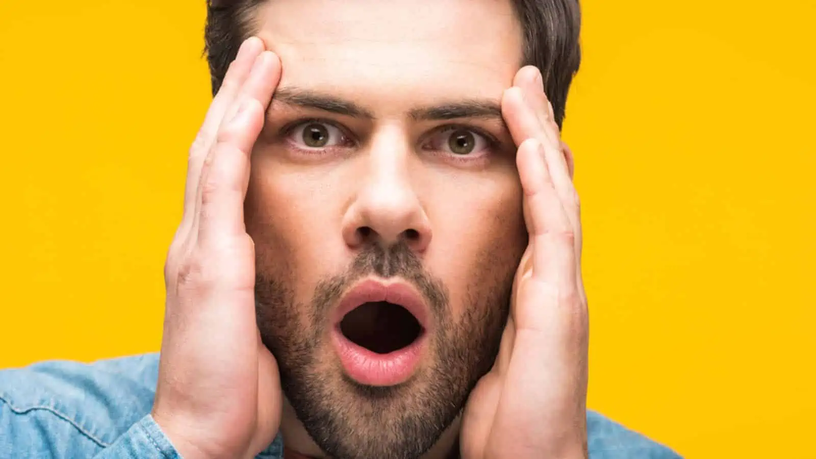 Shocked handsome man with hands on head isolated on yellow