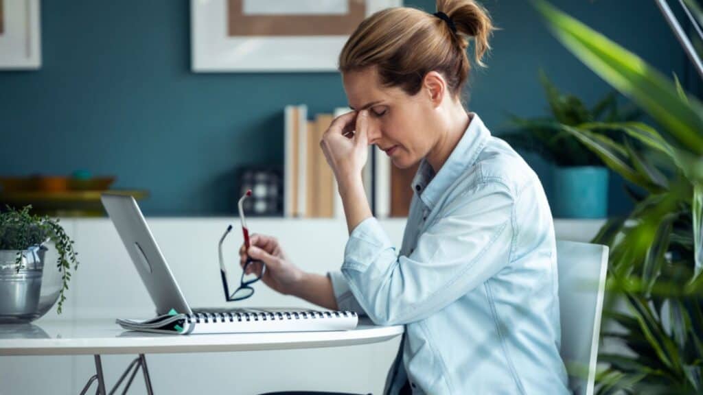 Shot of exhausted mature woman with headache while working with computer in the living room