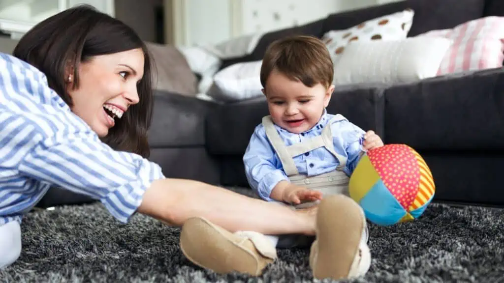 Shot of happy young mother with her baby boy playing on the floor of living room