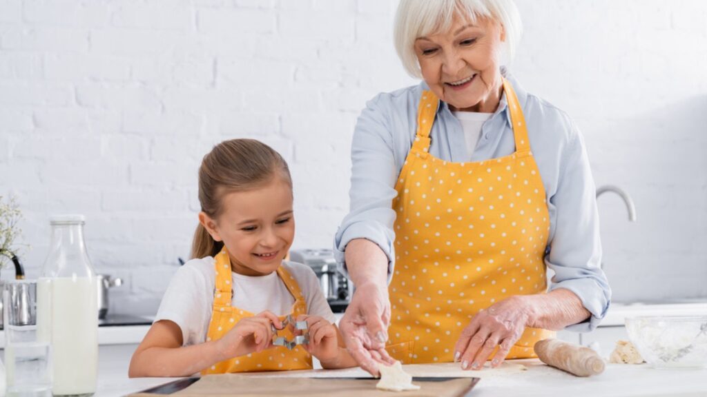 Smiling little girl holding cookie cutter near grandmother with baking