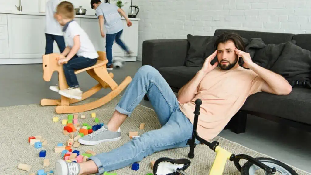 Stressed father sitting on floor and kids playing around in room