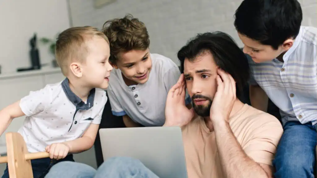 Stressed father with laptop and little kids around at home