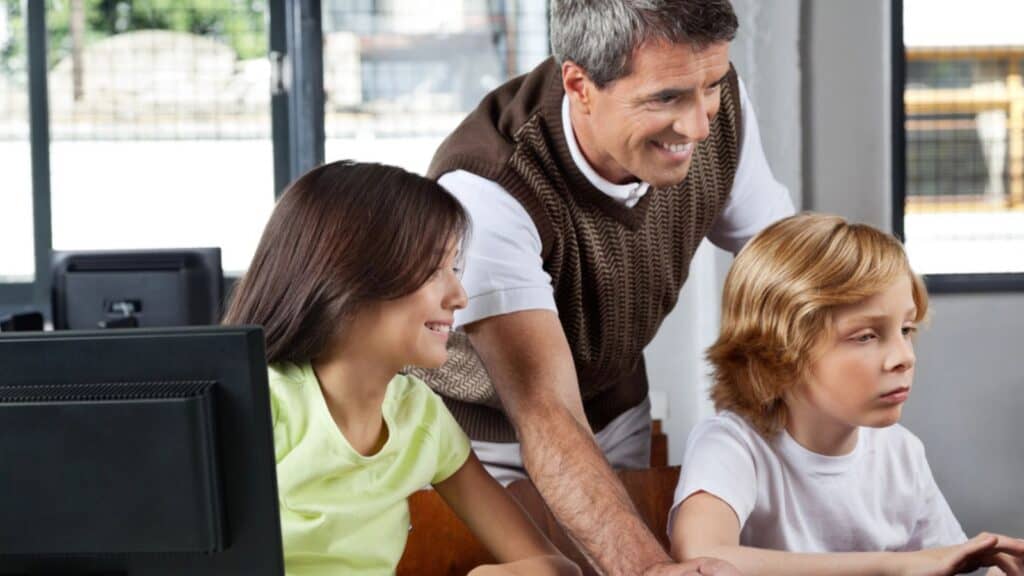 Teacher Assisting Schoolchildren In Using Desktop Pc