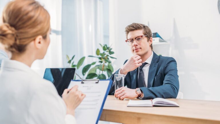 Thinking man in glasses sitting near recruiter with clipboard on job interview