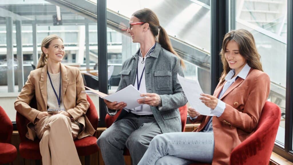 Three cheerful team members sitting on red chairs and discussing paperwork