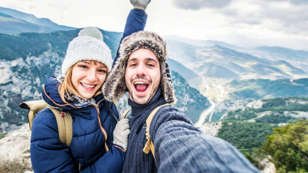 Traveler couple with backpacks taking selfie portrait hiking mountain