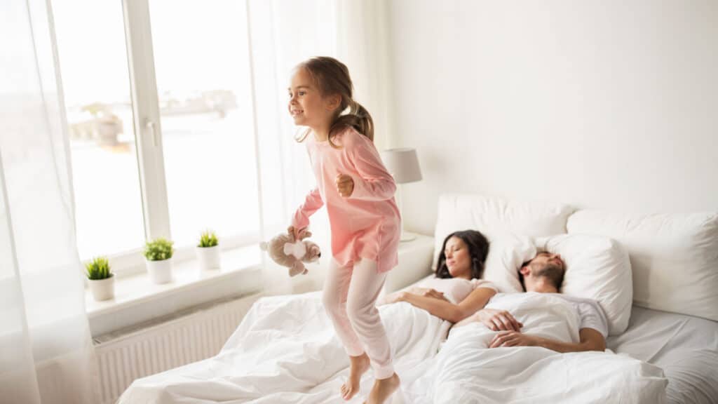 girl jumping on the bed tired parents white sheet sleep