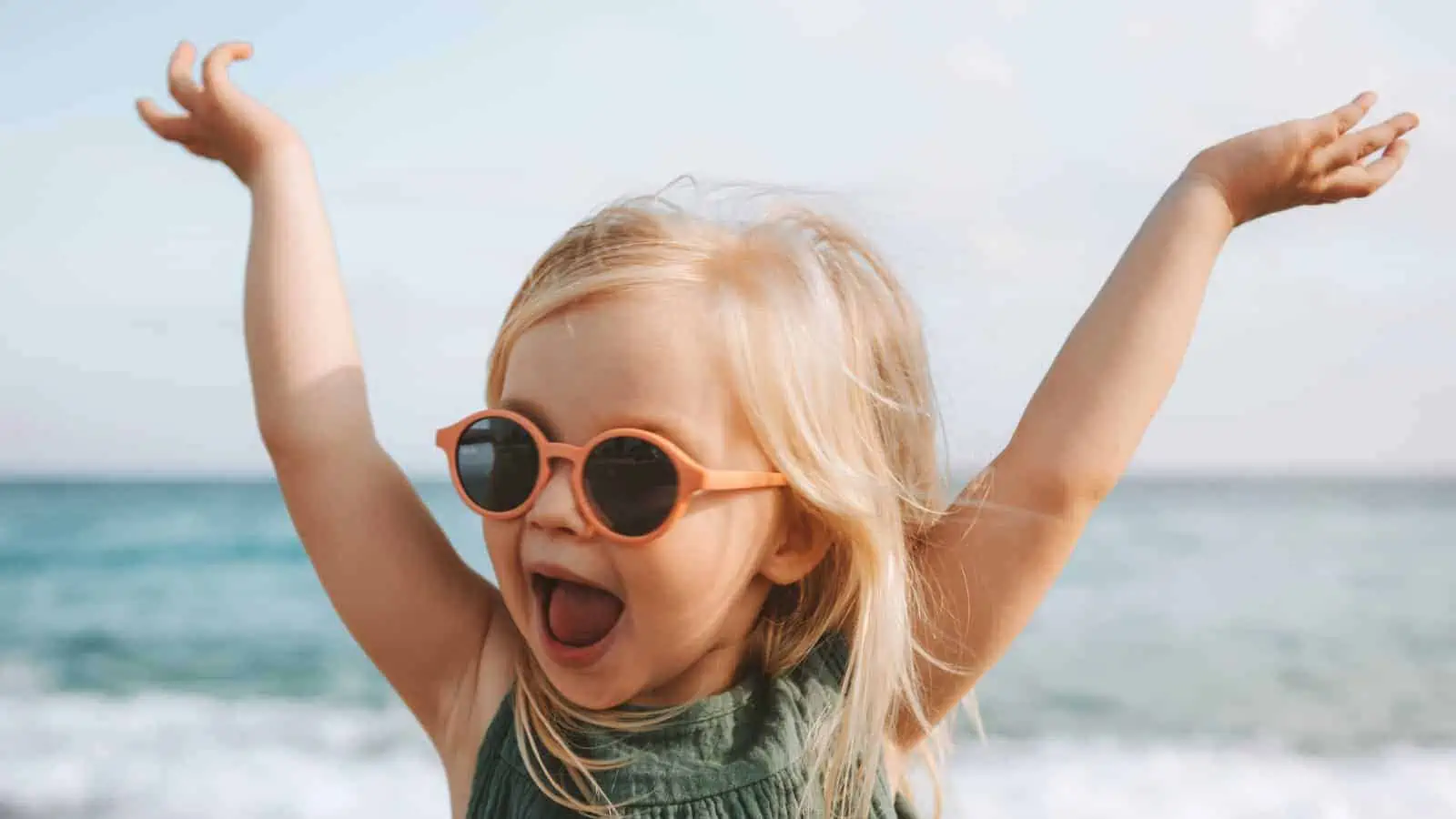 little girl happy at the beach sunglasses arms up laughing smiling