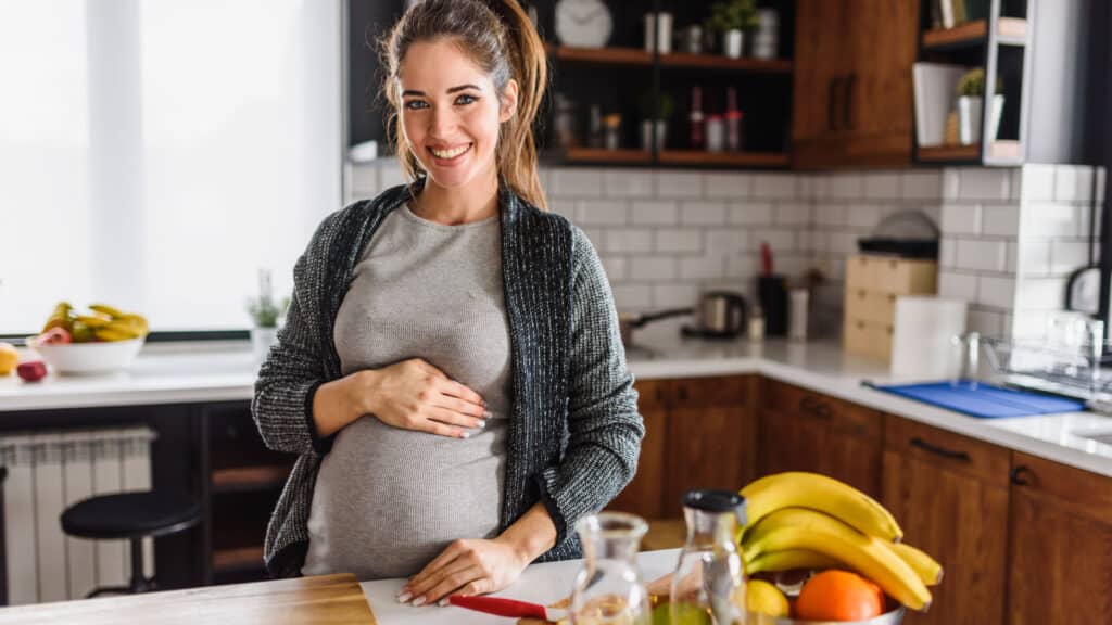 happy pregnant woman eating healthy food in kitchen