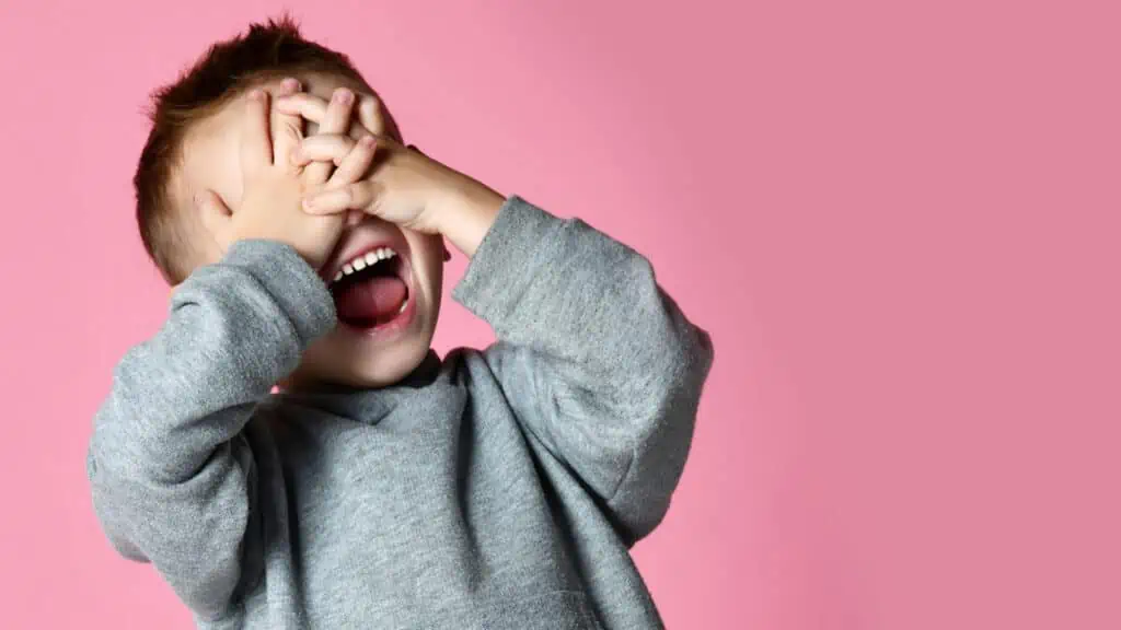 boy laughing and covering his eyes