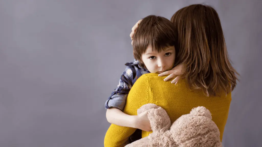 sad boy hugging his mom with a teddy bear