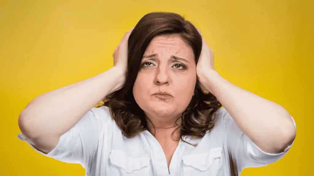 Unhappy stressed woman covering ears looking up in yellow