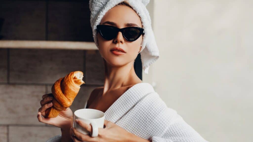 european woman eating a croissant and coffee with glasses and a towel in her robe