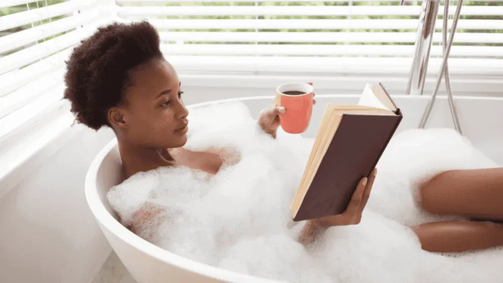 woman having a bubble bath reading a book coffee self care