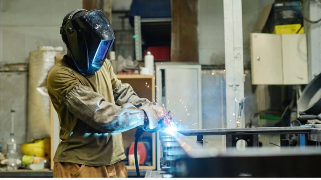 Welder in mask using torch to cut iron at his workplace in workshop