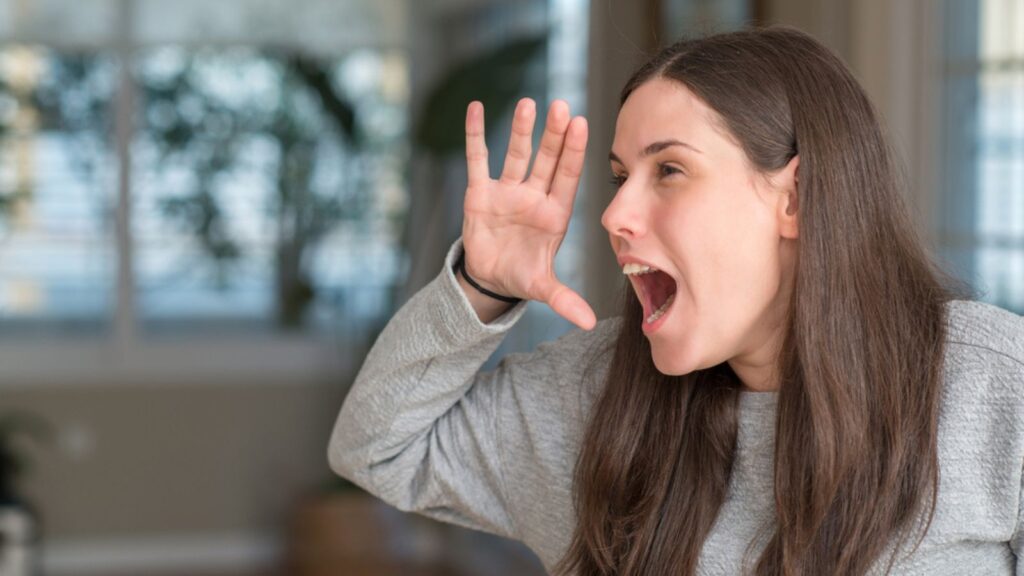 Woman at home shouting and screaming loud to side with hand on mouth