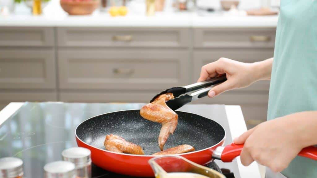 Woman cooking chicken wings in frying pan on stove
