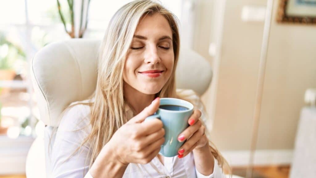 Woman mindful while drinking cup of coffee sitting on armchair at home