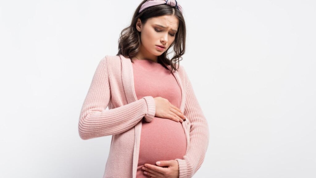 Worried pregnant woman in headband touching and looking at belly