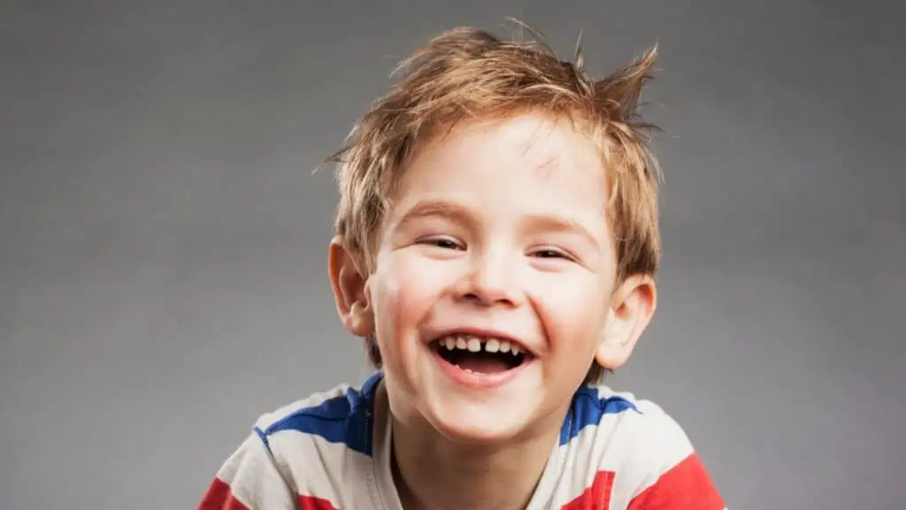 Young boy laughing against gray background