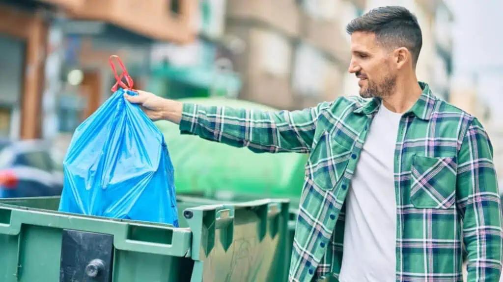 Young caucasian man throwing waste bag to the container at the city