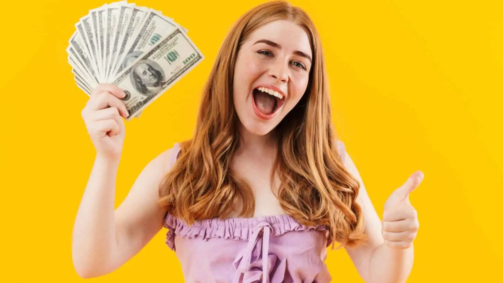 Young positive happy girl with money isolated over yellow wall background