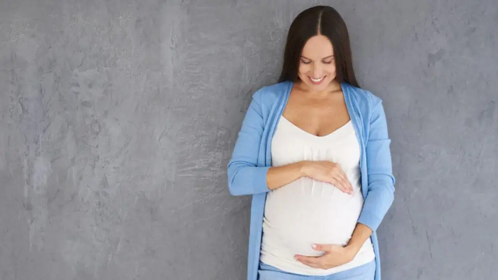 Young pregnant woman looking at her belly against grey background
