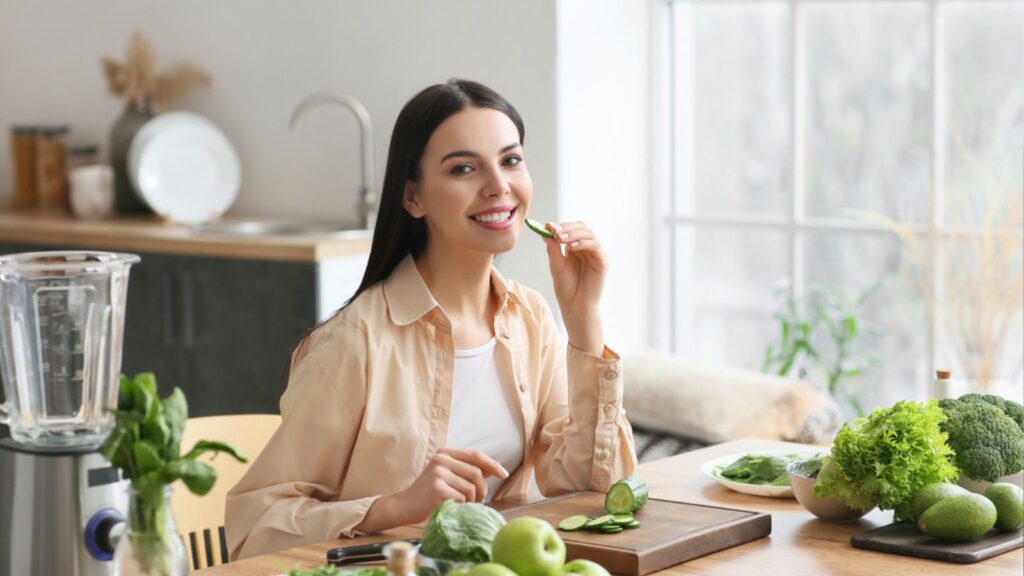 Young woman eating cucumber in kitchen