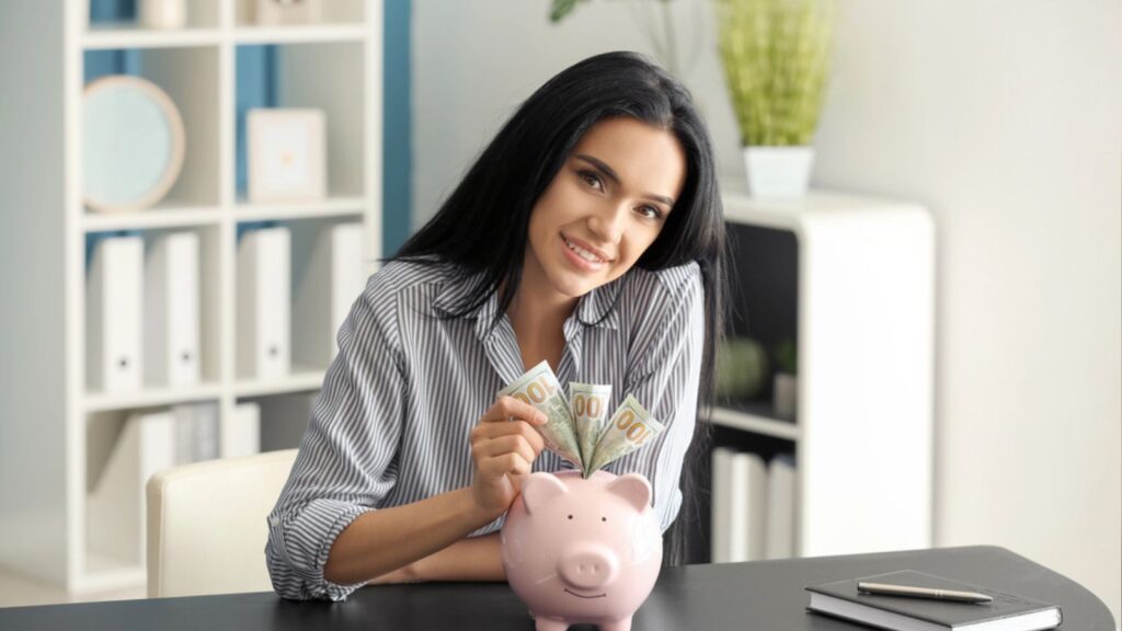 Young woman with money and piggy bank sitting at table