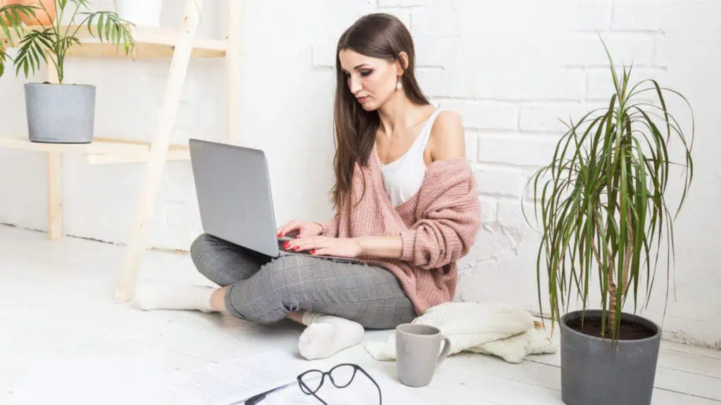 woman works at her computer at home sitting on floor plants