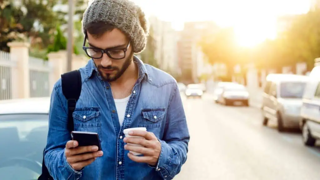 man holding a coffee and phone outside on the street