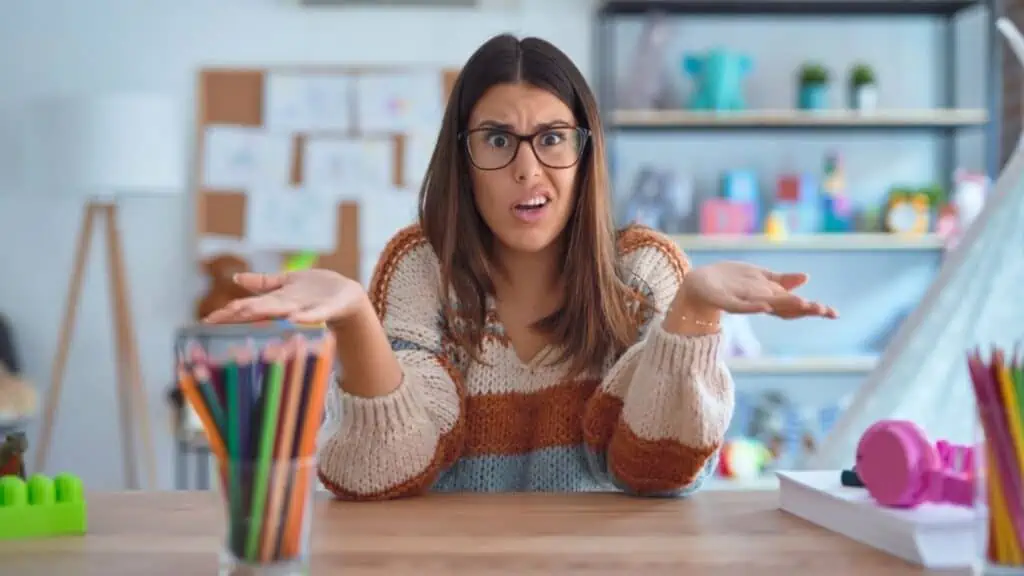 confused shocked teacher at a desk with colored pencils glasses