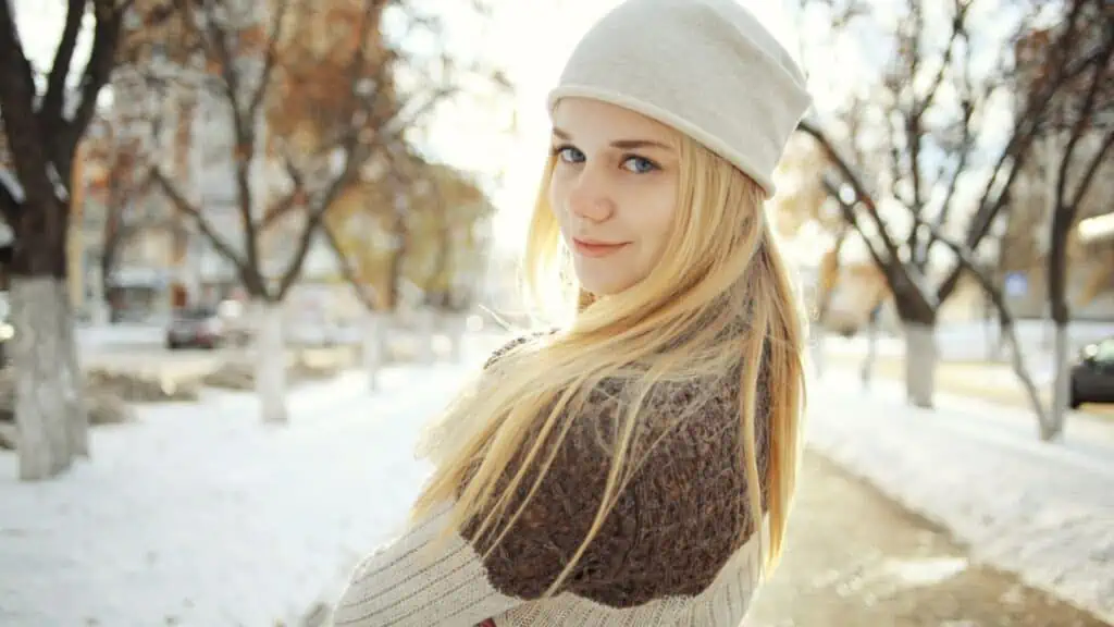 blonde girl in winter hat smiling snow